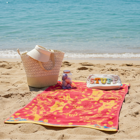 Beach scene with a colorful towel, bag, and toys on sand by the ocean
