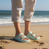 Pair of light green slides with gold buckles on a gray surface