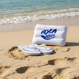 White inflatable pillow with blue 'AXA' logo and white flip-flops on a sand.
