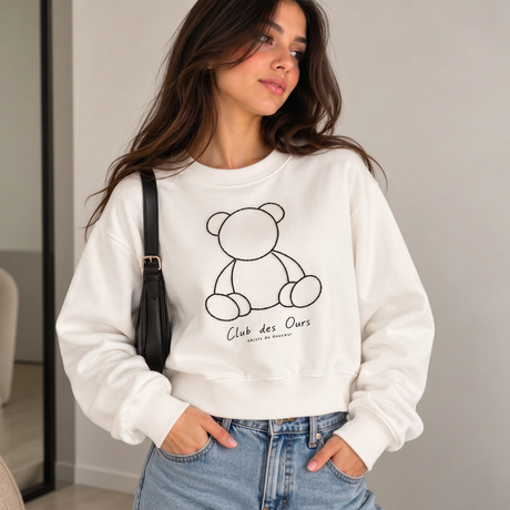 Woman in a white cropped sweatshirt with a black beaded teddy bear outline and jeans