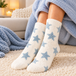 Fuzzy white socks with dusty blue stars worn on a cream rug beside a blue knit blanket