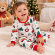 Smiling baby sitting on a fluffy rug in white Christmas pyjamas with red trucks, green trees and red cuffs