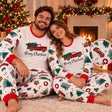 Smiling couple in matching white Christmas truck print pyjamas sitting by a fireplace