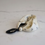 Cream-colored foulard with black ribbon and pearl on a marble surface