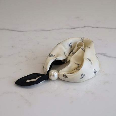 Cream-colored foulard with black ribbon and pearl on a marble surface