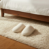 Empty ivory pair waiting on a shaggy rug beside a dark wooden bed frame