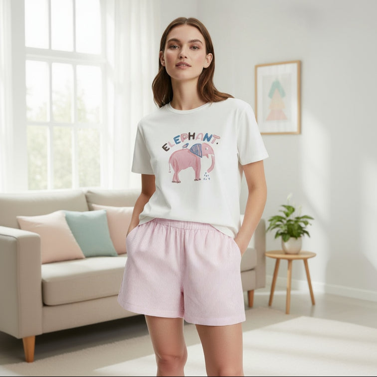 Woman wearing a white t-shirt with an elephant design and pink shorts in a bright room