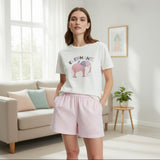 Woman wearing a white t-shirt with an elephant design and pink shorts in a bright room