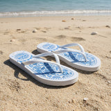 White flip-flops with blue floral patterns on a sandy beach