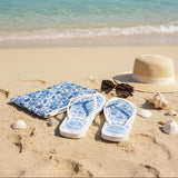Flip-flops with blue floral pattern on sand by the ocean