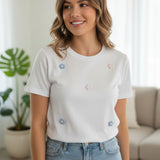 Woman wearing a white tshirt with floral embellishments in a living room setting