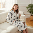 Smiling girl on a white sofa in a heart print robe, holding a cup