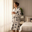 Woman standing by sheer curtains in a white robe with grey heart print and belt