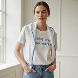 Woman wearing a white hydration tshirt with text and a white cardigan in a bright room