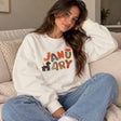 Woman in a white crew neck sweatshirt with colourful January lettering and a puppy print, sitting in jeans