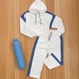 White hoodie and wide leg pants with blue stripes laid flat beside a blue water bottle