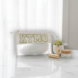 White pouch with 'KTMO' branding on a marble surface with cosmetic items