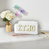 White pouch with 'KTMO' branding on a marble surface with flowers and jewelry