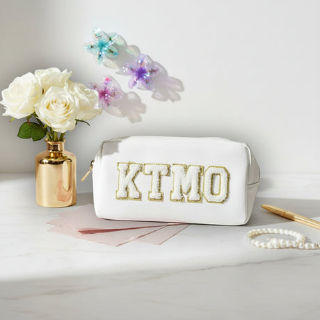 White pouch with 'KTMO' branding on a marble surface with flowers and jewelry