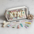 Clear white pouch with 'KTMO' branding, hair clips, and measurements 13x25cm on a light grey background