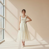 Woman in a white long skirt standing in a softly lit room with sunlight streaming through a window