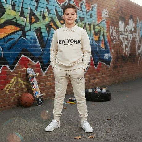 Boy wearing a cream New York collared sweatshirt and matching joggers beside a graffiti wall
