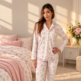Woman with a hand on her hip in a white rose print pyjama set, pink flowers on the bedside table