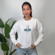 Woman wearing a white crew neck sweatshirt with a teal puppy scout graphic and light jeans