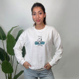 Woman wearing a white crew neck sweatshirt with a teal puppy scout graphic and light jeans