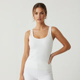 Woman wearing a white ribbed tank top against a plain background