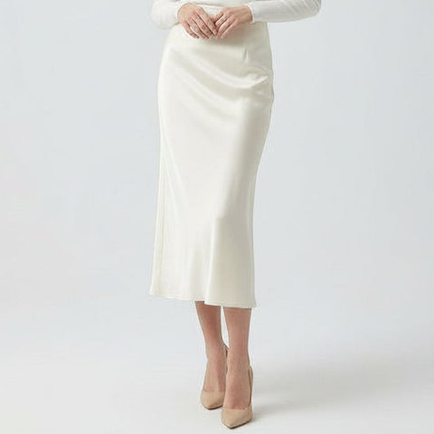 Person wearing a white skirt and beige heels on a plain background