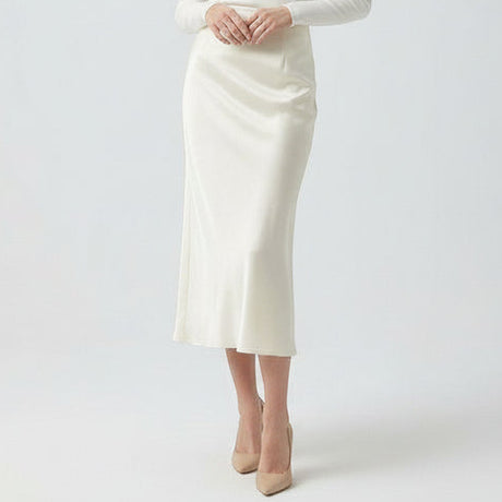 Person wearing a white skirt and beige heels on a plain background