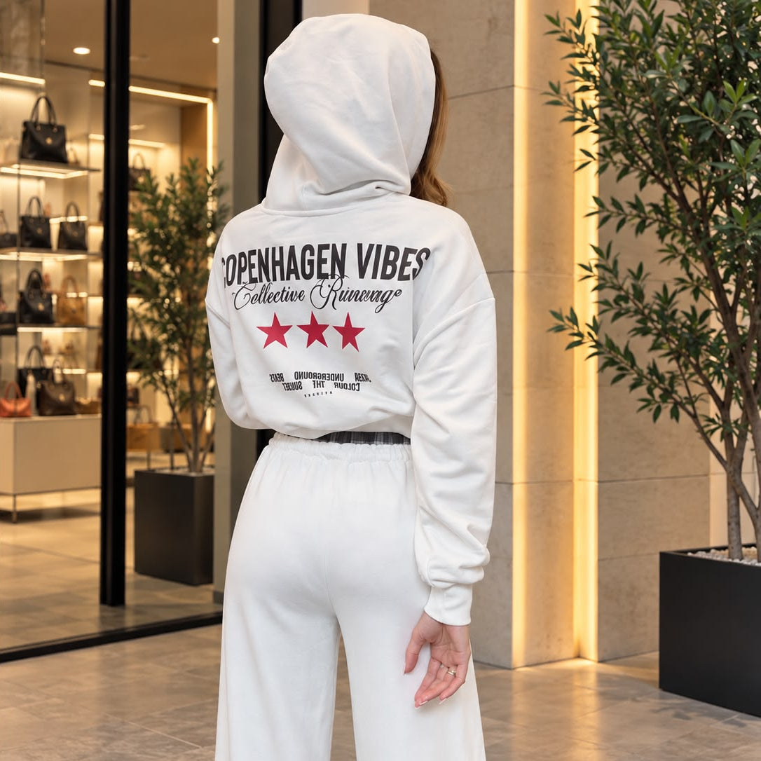 Back of a white cropped hoodie with a large slogan graphic and red stars, worn with wide leg pants