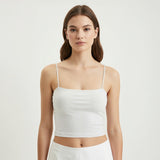Woman wearing a white tank top against a plain background