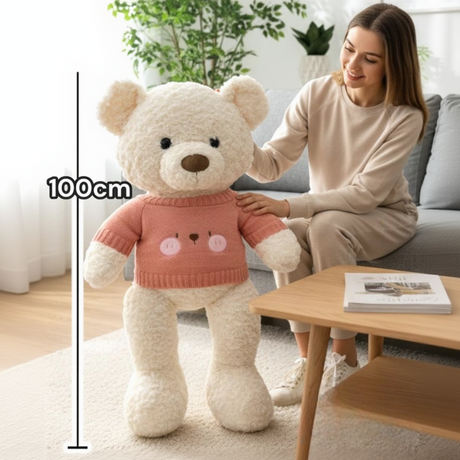 Ivory boucle teddy bear in a coral pink knit jumper beside a 100cm measuring line