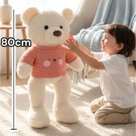 Kneeling child beside an ivory curly bear dressed in a coral pink knit top