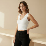 Woman wearing a white V-neck top and black pants against a beige background