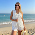 Woman in a white vest standing on a beach with ocean in the background