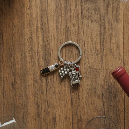 Wine keychain with bottle, corkscrew, grapes, and a red heart charm on wood