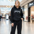 Woman wearing a black hoodie with 'Continue' text, and black sweatpants in a mall setting