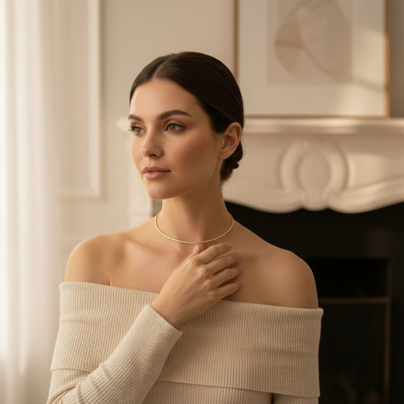 Woman wearing a beige off-shoulder sweater and gold necklace indoors