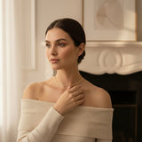 Woman wearing a beige off-shoulder sweater and gold necklace indoors