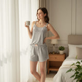 Woman in grey cami top and grey star-print shorts holding a mug in a bedroom setting