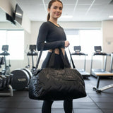 Woman holding a black duffel bag in a gym setting