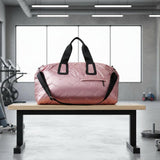 Pink duffel bag with black straps on a wooden bench in a gym setting