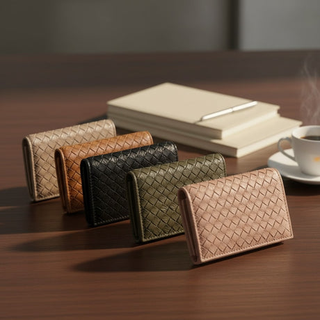 Set of woven leather wallets in various colors on a wooden surface with a notebook and coffee cup in the background.
