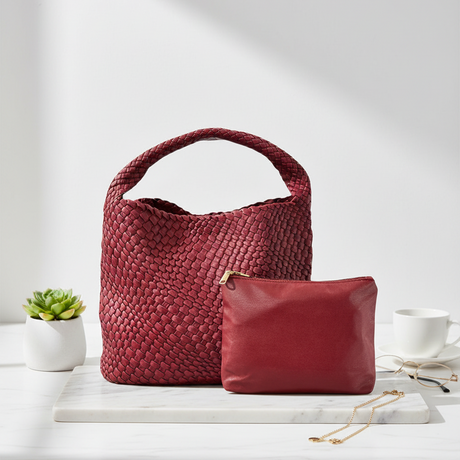 Red woven handbag and matching pouch on a white surface with a plant and cup in the background