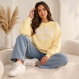 Woman sitting in a pale yellow Belleville Paris sweatshirt with white lettering and wide jeans