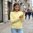 Woman in a yellow brushed wool crew neck sweater and light jeans adjusting her cuff outside a stone building