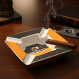 Square ashtray in yellow and black carbon dot ceramic, four white cigar rests along a gold rim